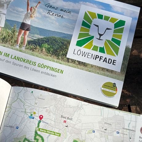 Offene Wanderbroschüre des Löwenpfad-Projekts im Landkreis Göppingen mit dem Slogan 'Ganz mein Revier.' und dem Logo. Darunter liegt eine detaillierte Wanderkarte mit markierten Routen und Orten wie Bad Boll und der Berta-Hörnle-Tour.